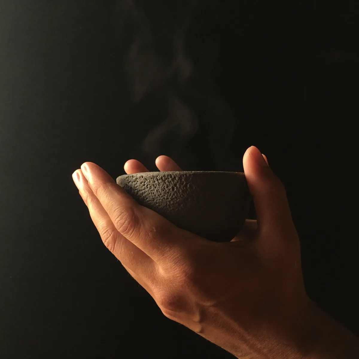 Unas manos sosteniendo una taza de cerámica humeante a contraluz